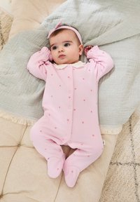 Helles rosa Babystrampelanzug mit kleinen rosa Herzmustern, einem weißen Kragen und Füßchen, auf einer strukturierten hellgrauen Decke ausgelegt.