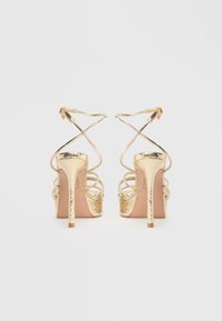 Sandale metalice aurii cu toc înalt, bretele încrucișate, accente texturate și o formă elegantă. Prezintă un toc stiletto înalt și spate deschis.