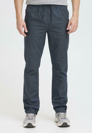 Pantalons de sport bleu marine avec une taille à cordon, un design fuselé et un motif texturé subtil. Associés à des baskets gris clair.
