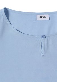 Lichtblauwe top met korte mouwen, ronde halslijn, enkele knoopsluiting en subtiele textuur. Label zegt "CECIL."