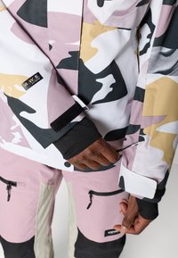 Kamalndumusteriga jakk roosa, valge ja kollase värviga mustade detailidega. Omab reguleeritavaid mansette ja mitu taskut sobivates roosades pükstes.