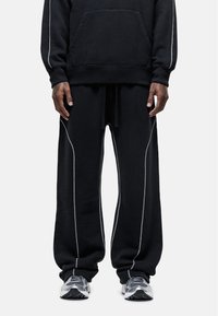 Zwart sweatshirt en joggingsbroek set gemaakt van zachte stof, met contrasterende witte stiksels langs de naden en een voorkant zak.