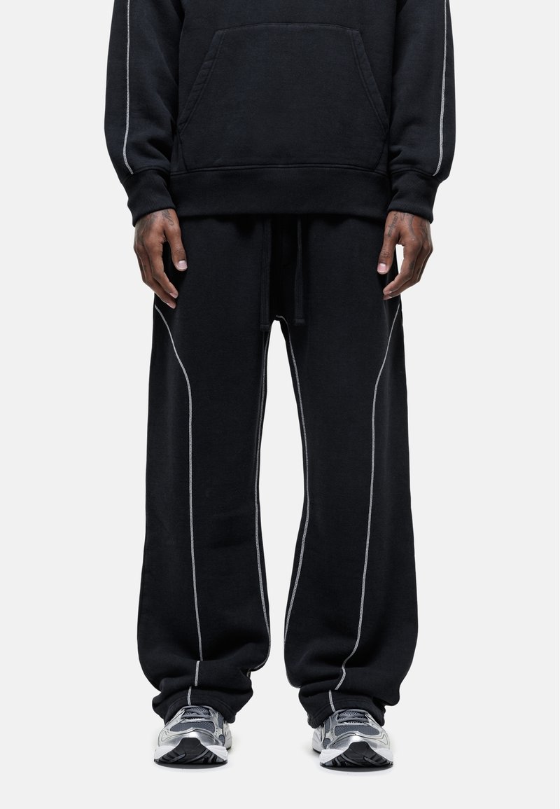 Zwart sweatshirt en joggingsbroek set gemaakt van zachte stof, met contrasterende witte stiksels langs de naden en een voorkant zak.