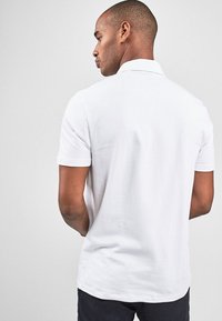 Hvid kortærmet poloshirt med klassisk krave, glat tekstur og lige kant, vist bagfra mod en neutral baggrund.