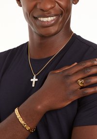Gold chain necklace with a silver cross pendant, gold bracelet with rectangular links, and gold ring with an embossed design on a dark shirt.