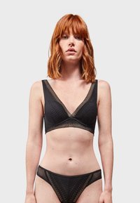 Bralette nera con design a scollo a V, caratterizzata da dettagli in rete testurizzata e spalline larghe. Abbinata a slip da bikini neri coordinati.