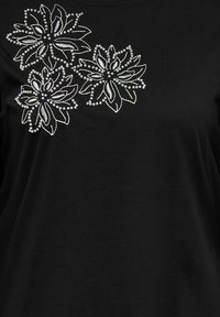 Czarna tkanina z białym haftowanym wzorem kwiatowym ozdobionym małymi perełkowymi koralikami po lewej górnej stronie.