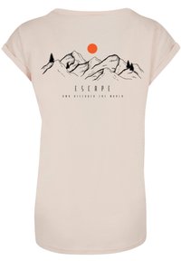 Light pink t-shirt featuring a black mountain graphic with trees and a red sun, text reads "ESCAPE AND DISCOVER THE WORLD" below.