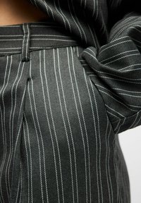 Tissu gris avec des rayures blanches ; gros plan sur un pantalon montrant la taille et les plis. Texture douce avec un design structuré.