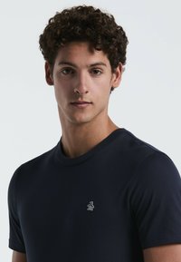 Marineblauwe t-shirt met korte mouwen gemaakt van een zachte katoenmix, met een klein wit pinguïnlogo op de linkerkant van de borst. Klassieke ronde halslijn.