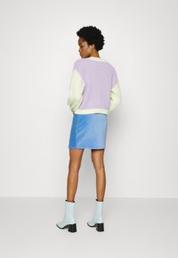 Suéter de malha com painéis em roxo e verde menta, combinado com uma mini saia em suede azul e botins de salto ligeiro azul claro.