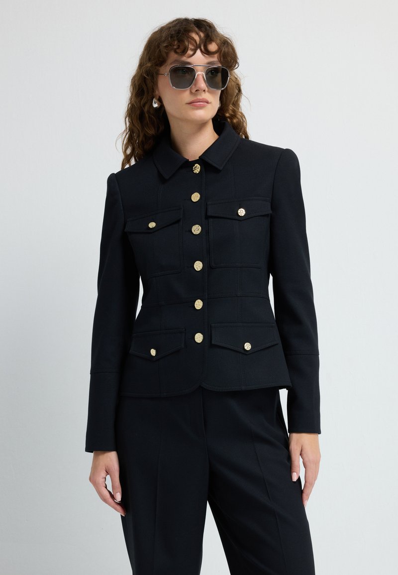 Czarna, dopasowana marynarka z złotymi guzikami, wieloma kieszeniami z przodu i kołnierzem. Gładki materiał o wyrafinowanym kroju.