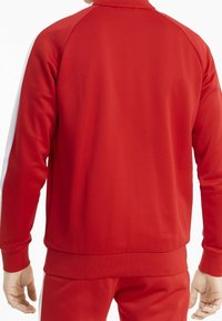 Giacca sportiva rossa realizzata in tessuto testurizzato, caratterizzata da un colletto alto e polsini a costine, con accenti bianchi sui lati e un design aderente.