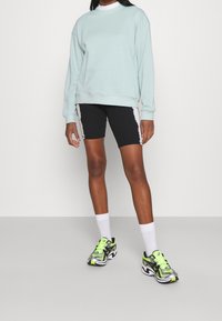 Ljusblå sweatshirt, svarta cykelshorts med vita sidostrippar och flerfärgade sneakers med reflekterande detaljer. Vita ankelstrumpor.