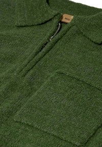 Grøn, struktureret fleece zip-up trøje med krave og stiklap lomme på venstre side, der har lynlås lukning. Brandmærke synligt indeni.
