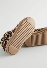 Sneakers w nadrukiem w panterkę, wykonane z miękkiego futra, z beżową gumową podeszwą z wgłębieniami, zapewniającą przyczepność i wsparcie.