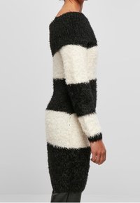 Robe en maille duveteuse avec des rayures horizontales noires et blanches. Comprend un décolleté bardot et une silhouette ajustée, atteignant le milieu des cuisses.