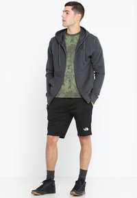 Hallide halli kapuutsiga jakke roheline kamuflaaž t-särk üleval, mustade lühikeste pükste ja logoga. Selga pandud mustade tossudega ja hallide sokkidega.