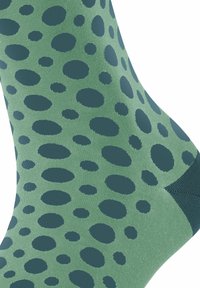 Grüne Socken mit einem Muster aus verschiedenen dunklen grünen Punkten, aus einem glatten Material mit einer gerippten Textur am Bündchen gefertigt.