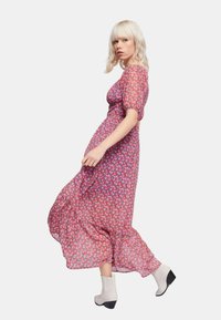 Abito maxi floreale con maniche a sbuffo corte, caratterizzato da una base rosa e motivi di fiori multicolori. Indossato con stivali alla caviglia color crema.