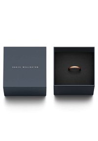 Kultaset rengas esillä tummansinisessä laatikossa, jossa on pehmeä musta sisustus. Laatikossa on kultaisella kirjailtuna "DANIEL WELLINGTON".