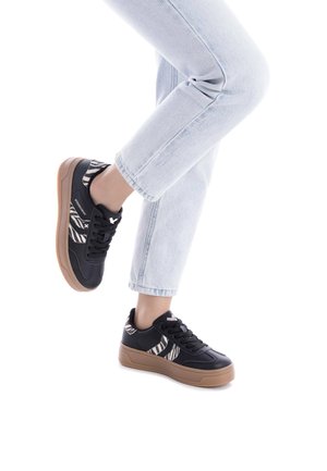 Zapatillas negras con acentos de estampado de cebra, material sintético texturizado y suela de goma marrón claro, combinadas con jeans de color azul claro.