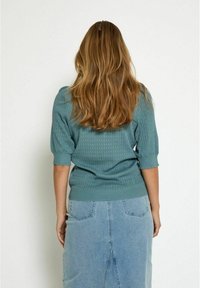 Türkiser Strickpullover mit kurzen gepufften Ärmeln und gerippten Bündchen, kombiniert mit einem hellblauen Jeansrock mit einem Schlitz hinten und seitlichen Taschen.