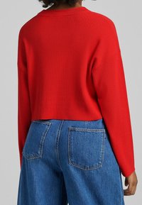 Czerwony prążkowany sweter o krótkim kroju i opuszczonych ramionach, dobrany do niebieskich jeansów z wysokim stanem z dwiema tylnymi kieszeniami.