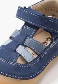 Scarpa in suede blu con accenti azzurri, punta chiusa e design con ritagli. Presenta cuciture bianche e una fascia in Velcro per una vestibilità sicura.