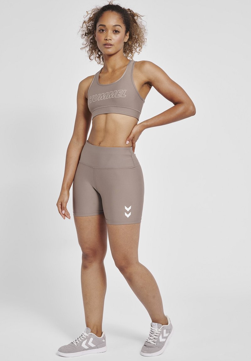 Sports bra and shorts set in beige with a smooth texture. Features a prominent brand logo and chevron accents in white.