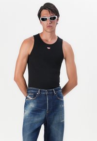Svart ärmlös linne med en liten röd logotyp, i kombination med blå denimjeans med en urtvättad finish och femficksdesign.