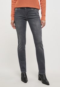 Vaqueros gris oscuro con un corte ajustado y un ligero desgaste. Combinados con botas negras de tobillo. Suéter naranja texturizado, con un cuello y puños acanalados.