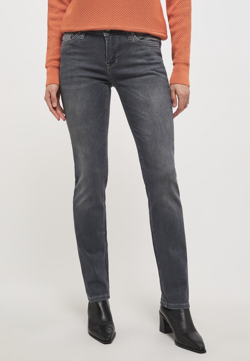 Vaqueros gris oscuro con un corte ajustado y un ligero desgaste. Combinados con botas negras de tobillo. Suéter naranja texturizado, con un cuello y puños acanalados.