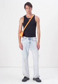 Zwarte tanktop, lichtblauwe spijkerbroek en zwarte sneakers. Een oranje schoudertas met een strak ontwerp hangt over de schouder.