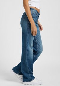 Jeans de pernera ancha en denim de color azul claro, con cintura alta, diseño clásico de cinco bolsillos y un ligero desvanecimiento a lo largo de las piernas.