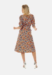 Floral-printed dress in orange and blue tones, featuring puff sleeves, a fitted waist, and a mid-length hem. Paired with silver high heels.