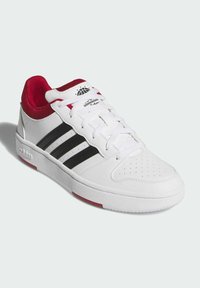 Białe sportowe buty z gładką skórzaną cholewką, trzema czarnymi paskami po bokach, czerwonymi akcentami przy kołnierzu oraz perforowanym noskiem dla wentylacji.