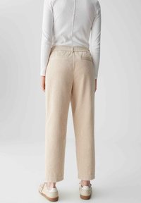 Beige Cordhosen mit lockerer Passform und elastischem Bund, ausgestattet mit Gesäßtaschen und einer strukturierten Oberfläche. Kombiniert mit weißen Sneakers.