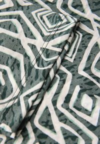 Tejido con estampado que presenta formas geométricas en verde oscuro y blanco. Textura suave con costuras visibles a lo largo de los bordes doblados.