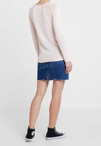 Un haut tricoté à manches longues rose clair associé à une jupe en denim effilochée. Des baskets montantes noires avec des accents blancs complètent la tenue.