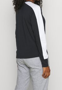 Top lungo nero a maniche lunghe con pannelli bianchi sulle spalle, caratterizzato da una vestibilità morbida e scollo rotondo. Abbinato a pantaloni della tuta grigi.