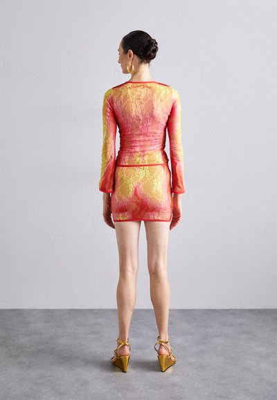 Lace dress set in gradient pink and yellow, featuring long bell sleeves and a fitted mini skirt. Paired with gold strappy heels.