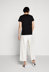 Camiseta negra de manga corta, combinada con pantalones anchos blancos con bolsillos de carga y sandalias de tacón alto en blanco con detalles a rayas.