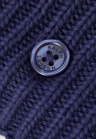 Marineblå strikket stof med hævet diagonalt ribmønster og en rund knap mærket "RALPH LAUREN" med fire huller. Blød tekstur.