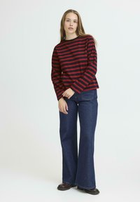 Red and navy striped long-sleeve top paired with flared dark blue jeans. The fabric appears soft, with a relaxed fit and standard crew neckline.