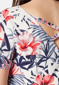 Blommig blus med röda och marinblå blommor på en krämfärgad bakgrund, med en insvängd design och korsade band vid halsringningen.