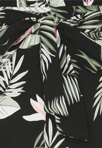 Tissu noir avec un motif de feuilles tropicales vertes, blanches et roses noué en un nœud à la taille.