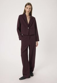 Burgunderfarbener, cropped Blazer mit einem einzigen Knopfverschluss und langen Ärmeln, kombiniert mit passenden, weit geschnittenen Hosen. Glatte Textur, formelles Design.