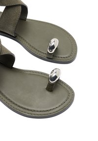 Oliwkowe sandały z gładką podeszwą, skrzyżowanymi zamszowymi paskami oraz metalicznym akcentem na pasku między palcami. Fakturowany i elegancki design.