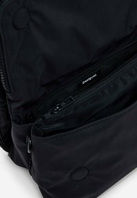 Black backpack with a smooth, matte nylon exterior. Features two zippered compartments and branded interior label. Subtle circular detail on fabric.